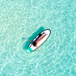 Aerial View of a Woman on a Surfboard in the Turquoise Waters of the Maldives